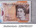 Small photo of Currency of Great Britain (England) pound. Banknotes with denomination and 10 images of Queen Elizabeth portrait on a gray background