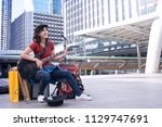Lovely Asian street girl musician playing guitar for donation on the sidewalk in city against city scape as background