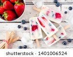 Healthy strawberry blueberry yogurt popsicles, top view summer table scene against a white wood background