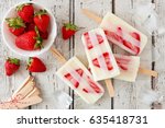 Group of homemade strawberry vanilla popsicles on a rustic white wood background
