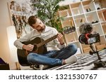 Learning guitar. Bearded male music blogger sitting on the floor at home and recording new guitar lesson for Youtube channel.