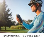 Hydration matters. Professional male cyclist holding water bottle, standing with his bike in park on a sunny day