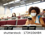 Small photo of education, healthcare and pandemic concept - african student girl wearing face protective medical mask for protection from virus disease with smartphone at lecture
