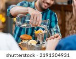 food, leisure and people concept - happy smiling man having dinner at restaurant and pouring water from jug to glass