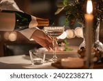 holidays, dinner party and celebration concept - close up of hand pouring champagne from bottle to glass on table at home or restaurant