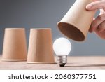 Small photo of Closeup hand reveal where the light bulb is in three cups shell game, helpful tips, reveal the success idea concept, or FAQs