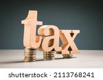 Small photo of Big wooden alphabets of TAX word on a small and a few heap coins, tax burden, tax time, lower money by tax