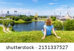 Girl in Olympic Park, Munich, Germany. Young woman sits on grass in Munich amusement district, person rests in summer. This place is tourist attraction of Munchen city. Travel people in Europe.