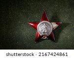 Red Star order on green uniform material background, Russia. Old Russian military medal to hero. High national Soviet army award in World War II. Concept of honor, patriotic and wwii victory symbol.