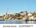 Winterized sloop rigged yachts and cutters moored to a snow-covered pier. Port crane in the background. Norway. Nautical vessel, transportation, sport, recreation, leisure activity, service
