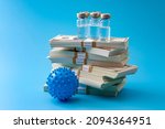 Small photo of Big pharma profiteering, healthcare corruption and pharmaceutical industry greed concept with vaccine vials on top of huge pile of money and coronavirus model isolated on blue background