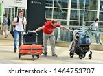 Small photo of Denver, CO, USA. July 27, 2019. Young man at Denver International Airport struggling to keep control of his luggage cart and baby buggy at the same time.