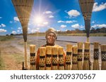 Small photo of African woman street vendor selling broomsticks by the side of the road