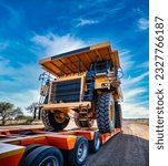 Small photo of heavy haulage huge yellow mining truck in top of a trailer on a dirt road