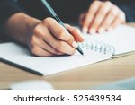 Close up of woman's hands writing in spiral notepad placed on wooden desktop with various items