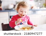 Small photo of Adorable baby girl eating from fork vegetables and pasta. food, child, feeding and development concept. Cute toddler, daughter with spoon sitting in highchair and learning to eat by itself.