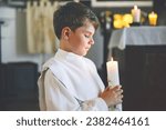 Small photo of Little kid boy receiving his first holy communion. Happy child holding Christening candle. Tradition in catholic curch. Kid in a white traditional gown in a church near altar.
