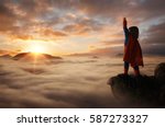 Little boy acting like a superhero on top of the mountain at sunset with copy space