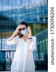 Small photo of Careworn woman wearing face mask and touching her head while standing outdoor and making a call.
