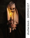 Small photo of Scary devilish possessed nun standing with a candle in a dark room. Horrors and Halloween.