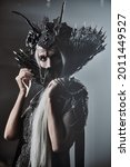 Small photo of A portrait of fabulous old woman with long gray hair, in a rich headdress and a rich black dress on a gray background. Black Queen, Witch. Halloween.
