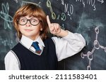 Small photo of Education. Portrait of a cute smart boy in neat school uniform wearing glasses standing at the blackboard with chemical formulas and holding his index finger up. Clever kids.