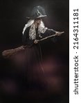 Small photo of Halloween. Full length portrait of an ugly old witch standing with her magic broom on a black backgroung. Witchcraft.