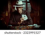 The criminal world of the mafia. A tough gangster man in an elegant black suit and a white hat sits in a luxury apartment and plays cards. Retro style. Detective movie.