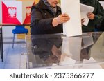 Small photo of ZARY, POLAND - 15 OCTOBER, 2023: Old woman puting a card with a vote to the ballot box during parliamentary elections. In the backround polish emblem.