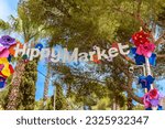 Small photo of Entry sign to the Punta Arabi hippy market in Es Canar, Ibiza, Spain. The sign is decorated with colorful paper flowers. Punta Arabi is the oldest and biggest hippy market in Ibiza.