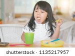 Small photo of Asian children or kid girl enjoy eating bread dessert and stick in one's throat with choke food or puke with colorful plastic dish and cup for baby on table in restaurant for breakfast or lunch