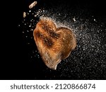 Flying toasted bread heart shape slice with crumbs explosion on black background 