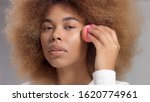 Small photo of Mixed race black woman with big afro hair in studio put a facial makeup base foundation on her cheek bone woman makes up