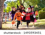 Child in Halloween costume. Mixed race Asian and Caucasian kids and parents trick or treat on street. Little boy and girl with pumpkin lantern and candy bucket. Baby in witch hat. Autumn holiday fun.