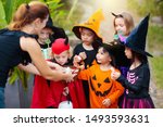 Kids trick or treat on Halloween night. Mixed race Asian and Caucasian children at decorated house door. Boy and girl in witch and vampire costume and hat with candy bucket and pumpkin lantern. 