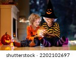 Little girl and boy in witch costume on Halloween trick or treat. Kids holding candy in pumpkin lantern bucket. Children celebrate Halloween at decorated fireplace. Family trick or treating.