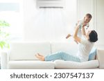Small photo of Asian mother and child with air conditioner remote control. Comfortable temperature at family home. Cooling device. Mom and baby boy on couch under cold breeze. Air conditioning on hot summer day.