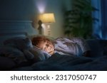 Small photo of Child sleeping in dark bedroom. Little boy napping. Healthy night rest. Kids room with night light. Toddler with teddy bear. Bedding for children.