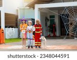 Kids trick or treat on Halloween night. Dressed up children at decorated house door. Boy and girl in witch and vampire costume and hat with candy bucket and pumpkin lantern. Autumn home decoration.