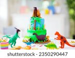 Small photo of Kids birthday party. Dinosaur theme cake. Little girl blowing candles and opening gifts. Children event. Decoration for dinosaurs themed celebration.