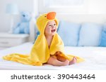 Happy laughing baby wearing yellow hooded duck towel sitting on parents bed after bath or shower. Clean dry child in bedroom. Bathing and washing of little kids. Children hygiene. Textile for infants.
