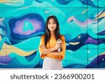 Smiling female street artist standing near the wall with her paintings holding spray paint can and looking to camera. Street art concept