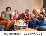 Group of friends eating popcorn and laughing while watching funny movie on TV at home