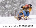 Beautiful young couple in love having fun spending winter vacation in mountains, sitting and hugging on sled, sliding down the hill in the snow