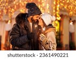 Small photo of Couple in love having fun celebrating New Year in the city streets, holding sparklers for midnight countdown with Christmas lights in background. Focus on the sparkler