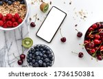 Fruits and berries breakfast delivery composition blueberry  raspberry cherries kiwi and mobile cellphone with blank screen for text copy space top view on white background