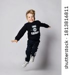 Small photo of Active frolic blond kid boy in black jersey sweater with printed words inscription on it jumps high over gray background. Translation: "Want. Can. Will Do"