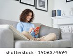 Small photo of Happy hispanic teen girl holding cell phone using smartphone device at home. Smiling young latin woman blogger subscribing new social media, buying in internet, ordering products online in apps.