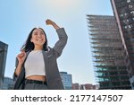 Young excited confident proud Asian business woman winner wearing suit standing on street, raising hands, feeling power, motivation, energy, celebrating career financial success in big city outdoors.