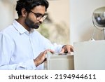 Small photo of Indian business man searching corporate documents in archive drawer. Files reference directory administrator accountant looking for papers, doing paperwork, organizing folders accounting storage.